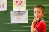 Foto Kind vor Tafel mit Kinderbildern zu Emotionen